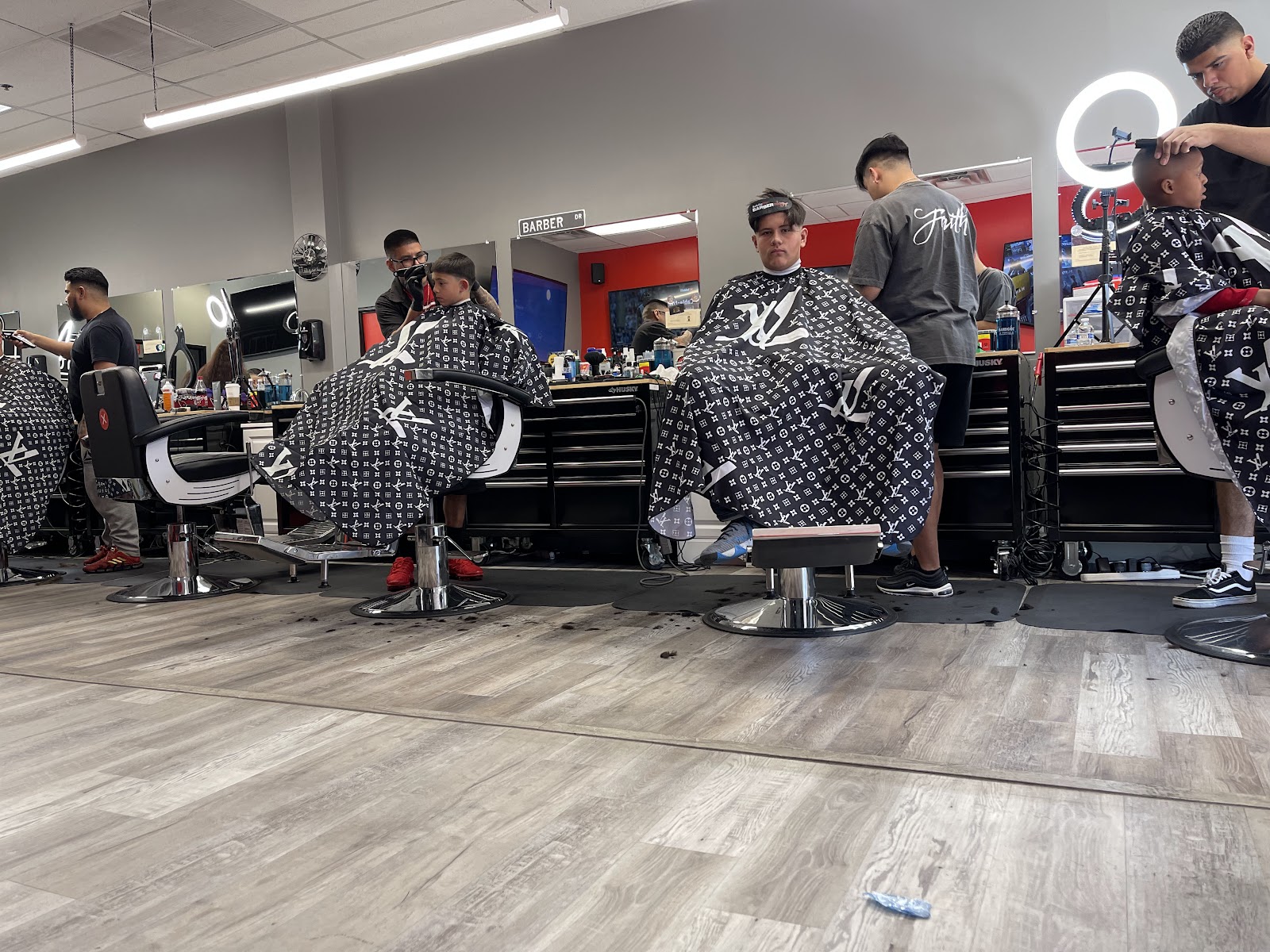 A weekday afternoon at Fresh Cuttz: four chairs going at once, kids and adults caped up in monogram capes, barbers working under the ring lights