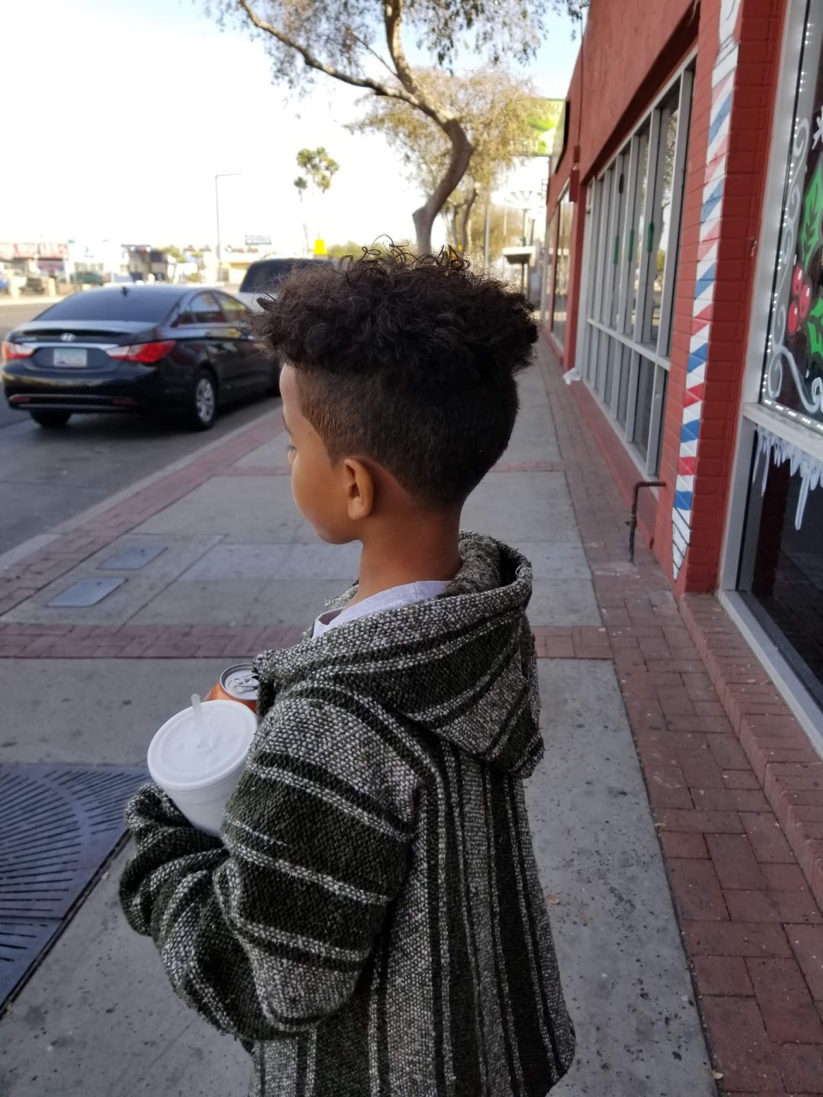 Young customer outside our red brick storefront on Glendale Ave with a fresh curly top fade